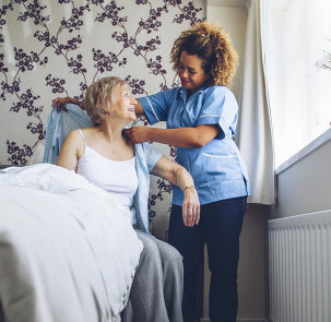 photo of a caregiver helping senior woman wear her blouse